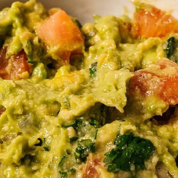 Close-up of chunky guacamole with visible pieces of avocado, tomato, and cilantro in a white bowl.