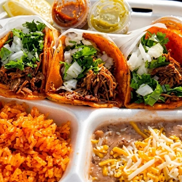 Three birria tacos with rice, refried beans, and sauces in a white takeout container.